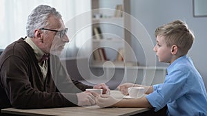 Happy little boy sharing news with grandfather, trustful family relations