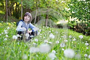 Happy little boy sitting dandelion on spring lawn among dandelion and green grass