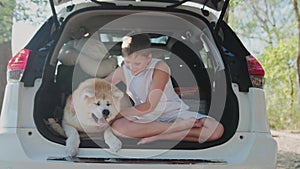 Happy little boy sitting with his dog in the open car trunk