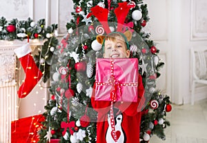 Happy little boy smiling with gift box near the Christmas tree.