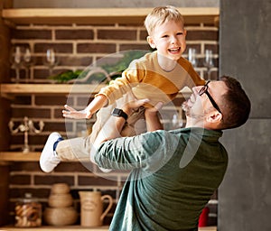 Happy little boy son playing with daddy at home, flying in air in fathers arms