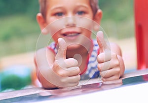 Happy little boy in a straped t-shirt shows the OK gesture at the playground.
