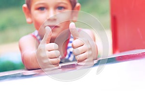 Happy little boy in a striped t-shirt shows the OK gesture at the playground