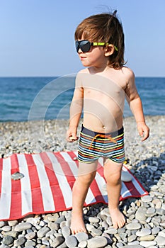 Happy little boy in sunglasses on stone beach