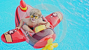Happy little boy swimming in blue street pool in courtyard. Joyful toddler, baby in sunglasses sitting in red inflatable