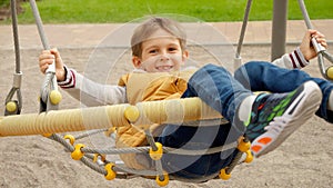 Happy little boy swinging in net rope swing at school playground. Active child, sports and development, kids playing outdoors