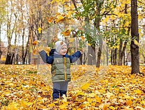 Happy little boy throws autumn foliage