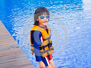 Happy little boy thumbs up with orange life jacket has fun and enjoy in the swimming pool