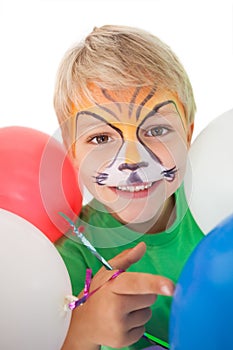 Happy little boy in tiger face paint with balloons