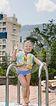 Happy little boy waving at the camera poolside