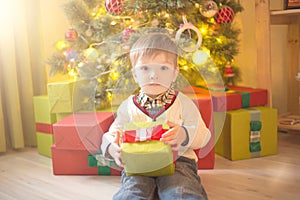 Happy little boy with Xmas present on Christmas Eve in decorated room. Sunny morning or day. Christmas or New Year