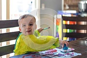 Cute toddler boy playing with paints at the kitchen table