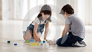 Happy little brother and sister playing with wooden multicolored bricks.