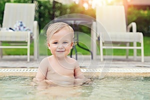 Happy little caucasian blond toddler boy swimming in wading pool on bright summer day at resort. Adorable baby enjoying