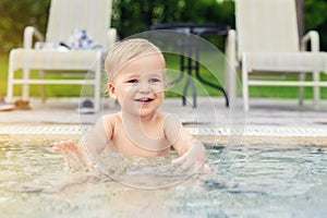 Happy little caucasian blond toddler boy swimming in wading pool on bright summer day at resort. Adorable baby enjoying outdoor