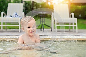 Happy little caucasian blond toddler boy swimming in wading pool on bright summer day at resort. Adorable baby enjoying outdoor