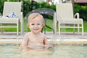 Happy little caucasian blond toddler boy swimming in wading pool on bright summer day at resort. Adorable baby enjoying outdoor