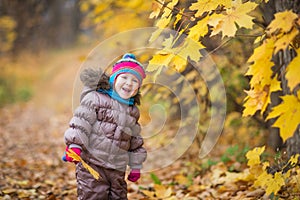 Happy little child, baby girl laughing and playing leaves in the autumn on the nature walk outdoors