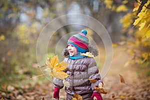 Happy little child, baby girl laughing and playing leaves in the autumn on the nature walk outdoors