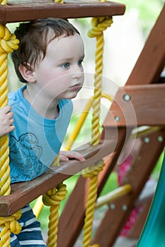 Happy little child boy climbing on the rope ladder outside