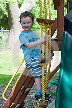 Happy little child boy climbing on the rope ladder outside