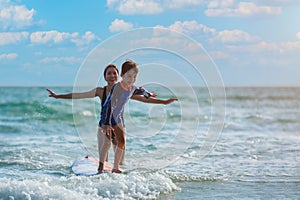 Happy little child boy learning to play surfboard from his mother with having fun and passion in sea on summer vacation at