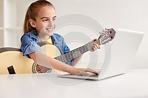 Cheerful girl with guitar using laptop photo