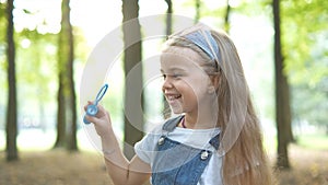 Happy little child girl blowing soap bubbles outside in green park. Outdoor summer activities for children concept