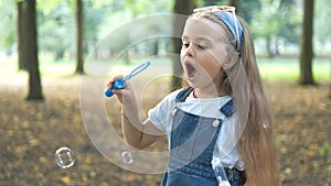 Happy little child girl blowing soap bubbles outside in green park. Outdoor summer activities for children concept