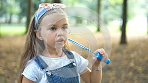 Happy little child girl blowing soap bubbles outside in green park. Outdoor summer activities for children concept