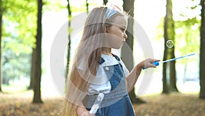 Happy little child girl blowing soap bubbles outside in green park. Outdoor summer activities for children concept