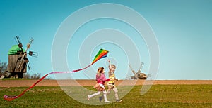 Happy little child girl and boy in front of windmills playing kite. Children running on the field. Renewable energies