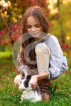 Happy little child girl with cute rabbit. Portrait of kid with pet. Outdoors