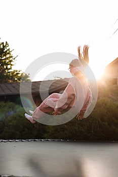 Happy little child girl having fun and jumps on trampoline outdoors, at backyard of the house on sunny summer day
