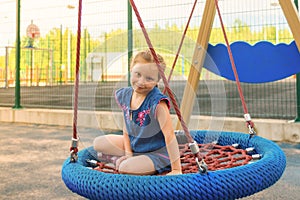 Happy little child girl laughing and swinging on a swing in the city park in summer