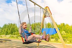 Happy little child girl laughing and swinging on a swing in the city park in summer