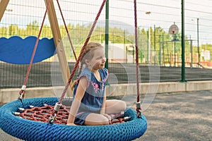 Happy little child girl laughing and swinging on a swing in the city park in summer