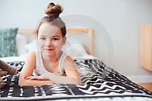 Happy little child girl lying on her bed in the morning, waking up in comfortable room with modern bedlinen