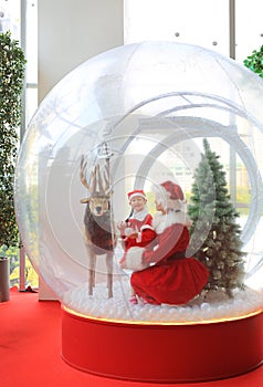 Happy little child girl and mother in santa costume dress has fun in big winter Snow globe with reindeer on christmas time. Merry