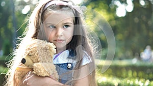 Happy little child girl playing with her favorite teddy bear toy outdoors in summer park