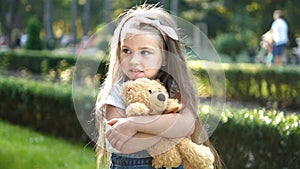 Happy little child girl playing with her favorite teddy bear toy outdoors in summer park