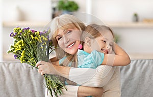 Happy little child greeting happy aged woman with flowers
