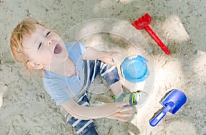 Happy little child having fun playing with sand and colorful toys in the park, beautiful summer sunny day in children playground