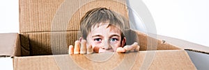 Happy little child hiding in a cardboard box, playing peekaboo