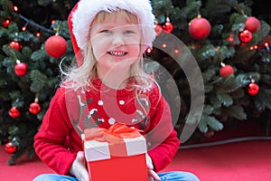 Happy little child kid girl in Santa red hat holding Christmas gift in hand.