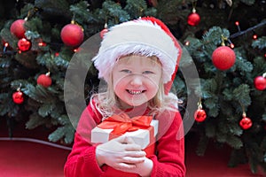 Happy little child kid girl in Santa red hat holding Christmas gift in hand.