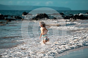 Happy little child running on the tropical beach. Boy playing sea waves on vacation sea in the summer holiday. Kid in