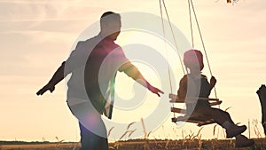 Happy little child with a teddy bear and dad is riding a swing at sunset in the park, playing the plane flying in the