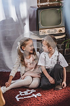 happy little children in 1950s style clothes playing with domino tiles