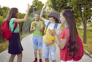 Happy little children with backpacks saying goodbye after school stand on path in summer park